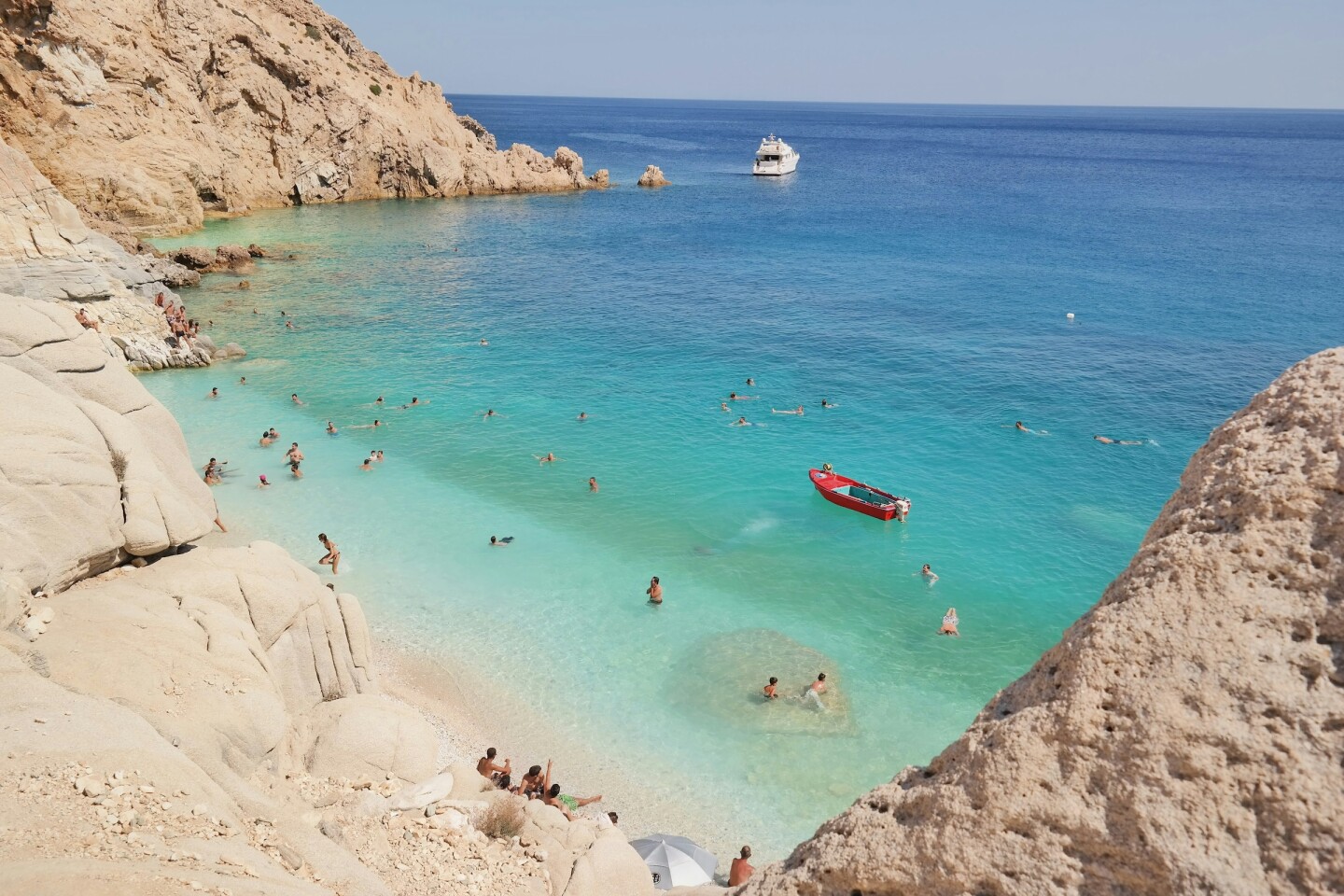 A horseshoe-shaped bay with crystal water, with boats and swimmers  