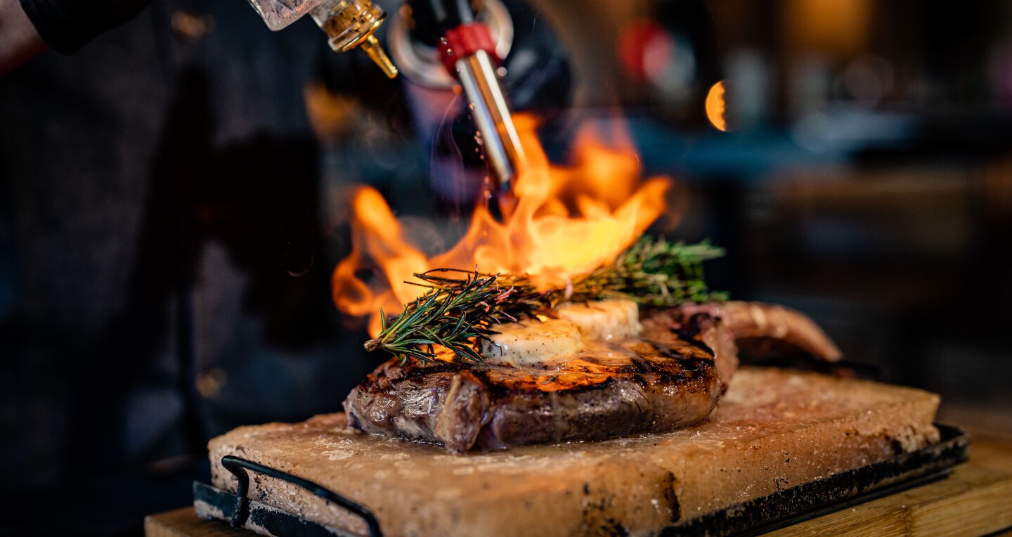 A steak covered in herbs being set fire by a blow torch at dLeña restaurant in Washington, D.C.
