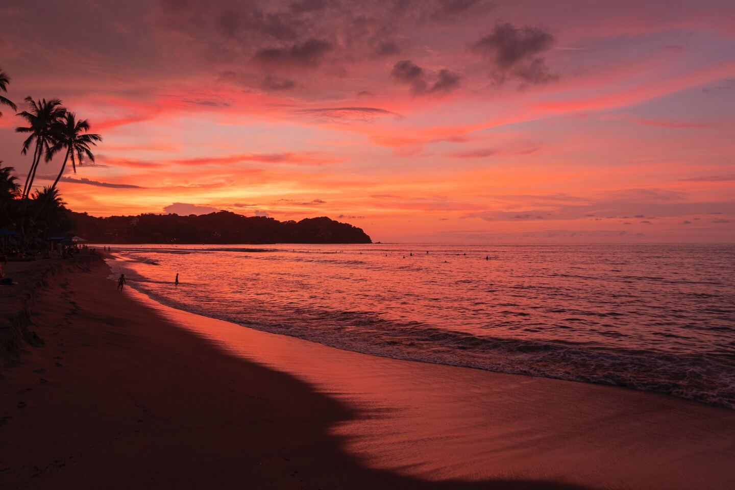 Sunset on a beach, two people walking by the water in background
