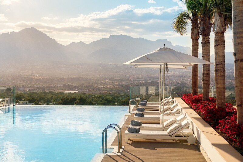 Infinity pool, with empty white lounge chairs; mountains in distance at Sha Wellness Clinic