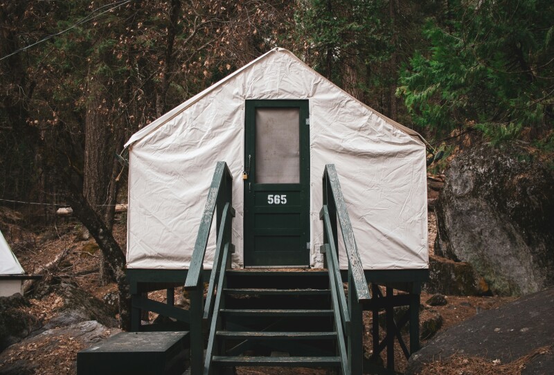 A frontal view of a white canvas tented cabin in Curry Village, Yosemite National Park, with steps leading up to a simple green door, the forest in the background