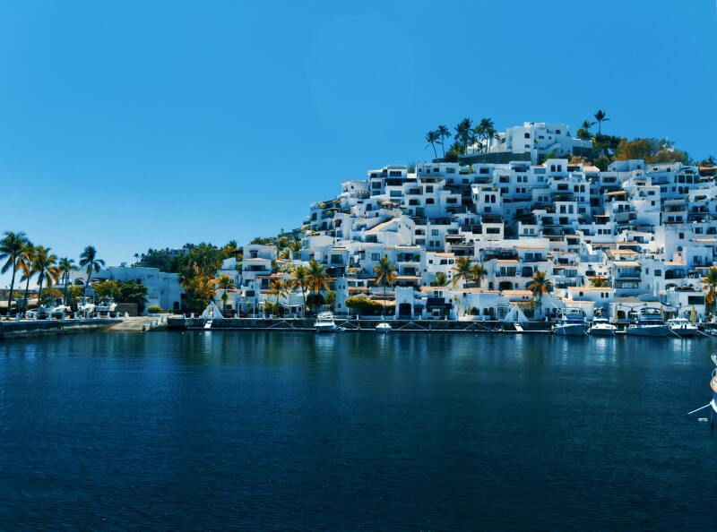 View of hillside white homes and buildings along the water in Manzanillo, Mexico