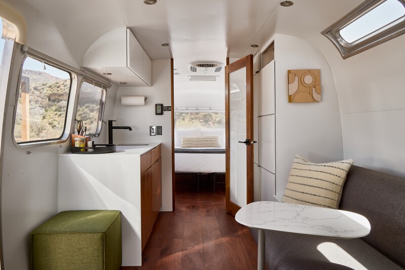 The interior of one of the trailers at AutoCamp Zion, showcasing the kitchenette, a living room sofa, with the bedroom through a door in the background.