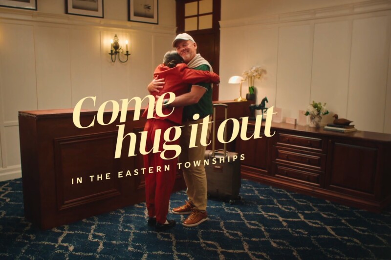 A hotel clerk and guest hug with the tag line "come hug it out in the Eastern Townships" overlaying the image