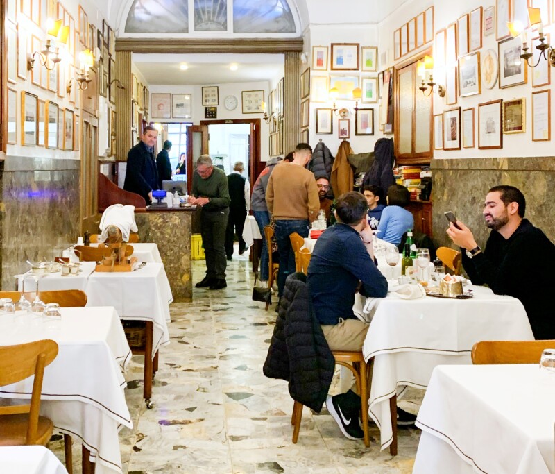 Narrow interior of historic restaurant, with several people at small square tables with white tablecloths