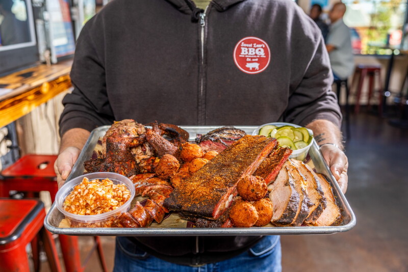 At Sweet Lew’s BBQ, the Super Sampler platter comes with brisket, chopped pork, ribs, a sausage link, whole jumbo wings, four sides, and hush puppies.