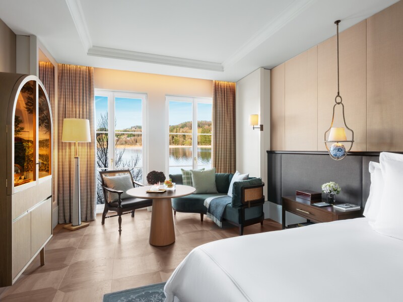 A modern guest room with wooden floors and walls, plus seating area next to large windows