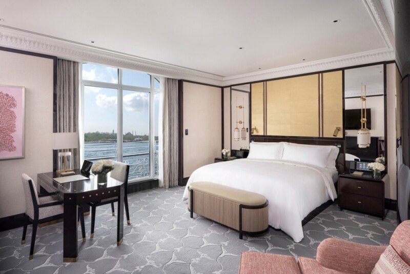 Guest room with modern furniture, gray patterned carpet, and large window overlooking water