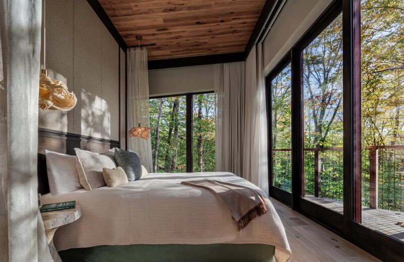 Beige bedroom of a tree-house accommodation at Twin Farms, with two walls of floor-to-ceiling windows and views of birch forest