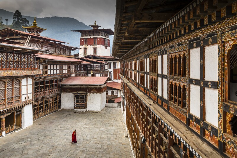 Monk in courtyard of a dzong fortress that is nestled in the Himalayan Mountains