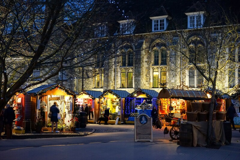 Several small vendors' huts lit at night, next to leafless trees and Winchester Cathedral