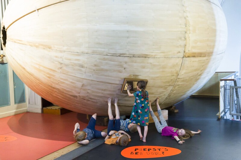 Several children next to large egg-shaped object indoors