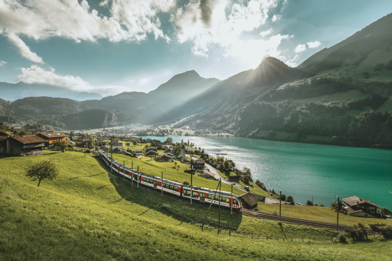 The Lucerne Interlaken Express train passes by a lake and a mountain.
