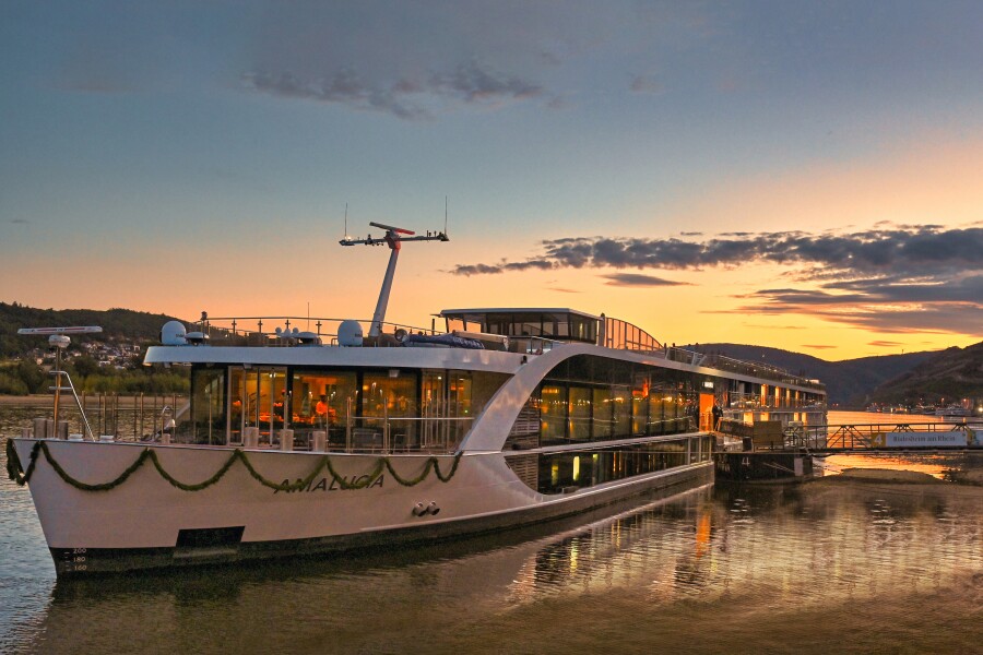 Exterior view of the 156-passenger 'AmaLucia' river cruise ship docked at sunset and with green garland decorating the bow of the vessel