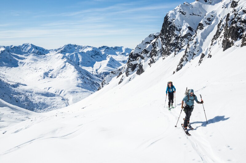 Two skiers skiing uphill on a hot sunny day in the Alaska backcountry of the Talkeetna Mountains.