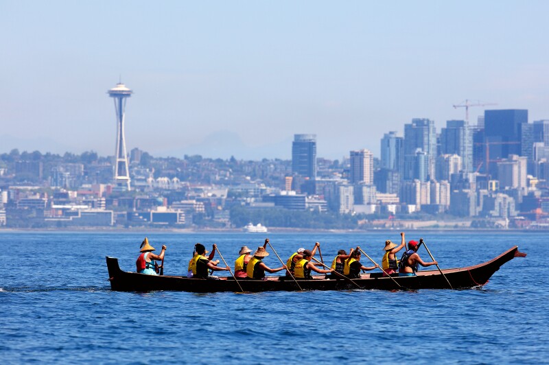 A group of Coast Salish people paddle a canoe in the Seattle harbor.