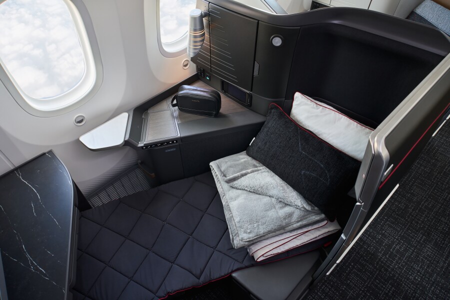 Overhead view of an American Airlines Flagship Suite with dark seat in a lie-flat bed position with gray, black, and white pillows and bedding folded atop