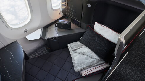 An overhead view of an American Airlines Flagship Suite with the seat in a lie-flat bed position with grey, black, and white pillows and bedding folded atop