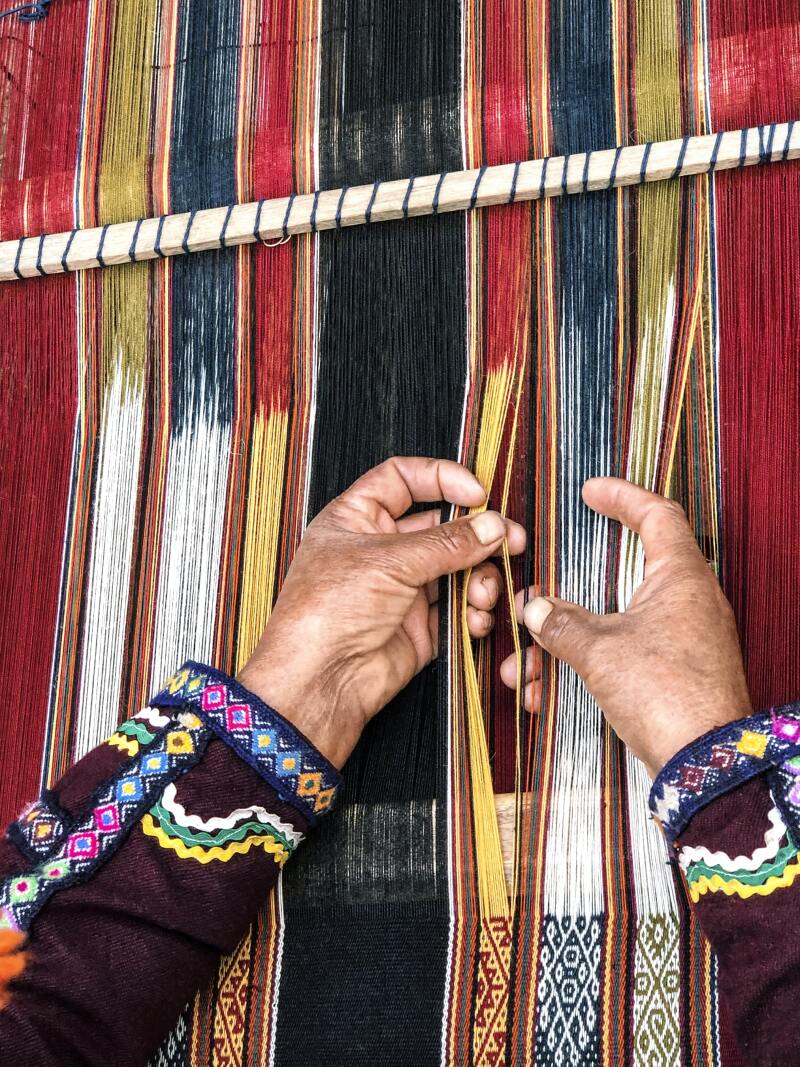 A weaver from the indigenous Amaru community works on a table runner.
