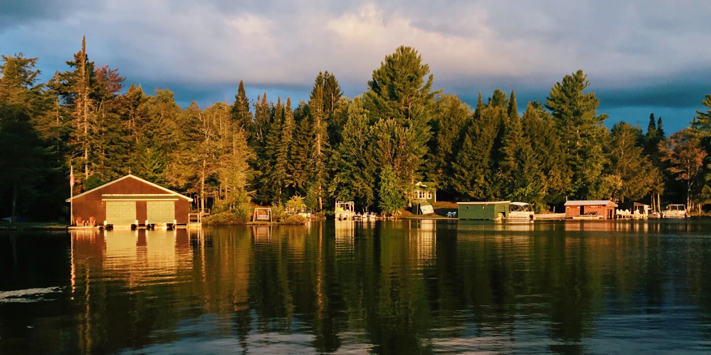 Boat houses along Seventh Lake in the Adirondacks, New York, with tall evergreen trees in background