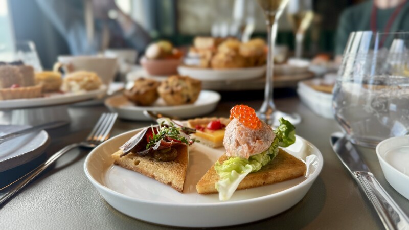 A Nordic afternoon tea spread at fine-dining restaurant Røst onboard 'MS Trollfjord' featuring smoked reindeer and Pacific salmon sandwiches and an assortment of scones, jams, cakes, and macaroons.