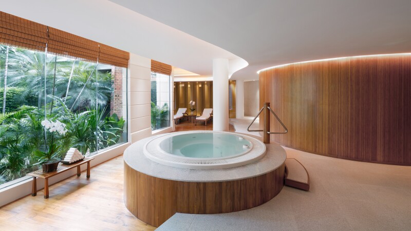 The relaxation area of the spa at Chiva-Som, with large whirlpool in center and wall of windows at left
