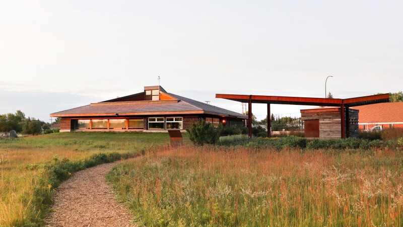 A footpath through a prairie at sunrise, with a low wooden building in background