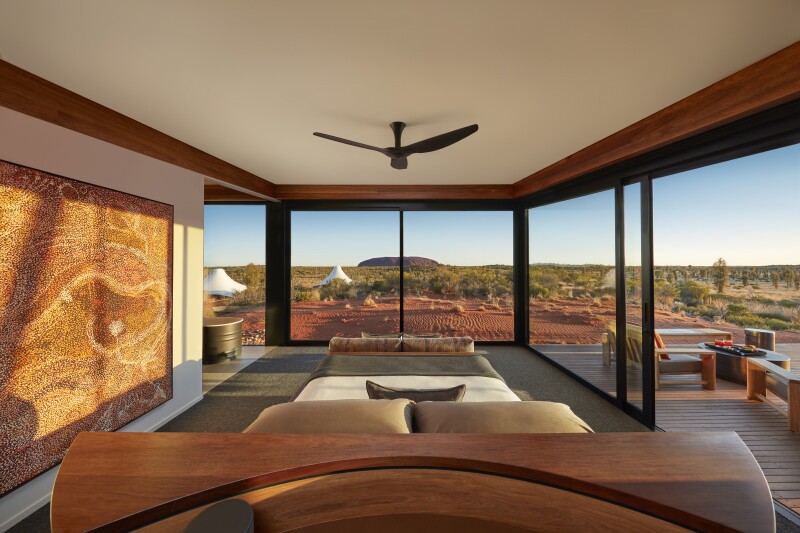A Dune Pavilion Bedroom at Longitude 131, with ceiling fan, two walls of windows overlooking scrubland, and patio