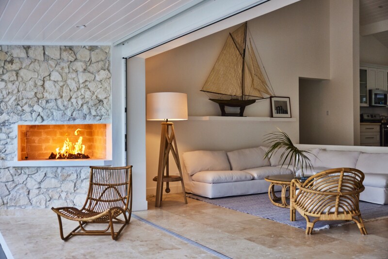 Guest accommodation with lit fireplace in white stone wall; large white sofa and two rattan chairs