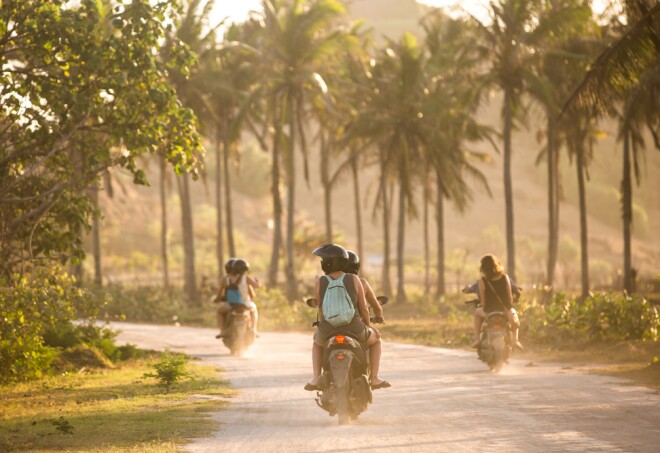Tourists travelling on scooters on a tropical island's dirt road