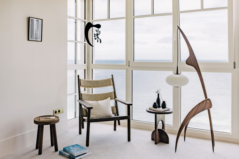 White guest room at Les Bassans, with modern furnishings and art (including small sculptures) and floor-to-ceiling windows facing sea