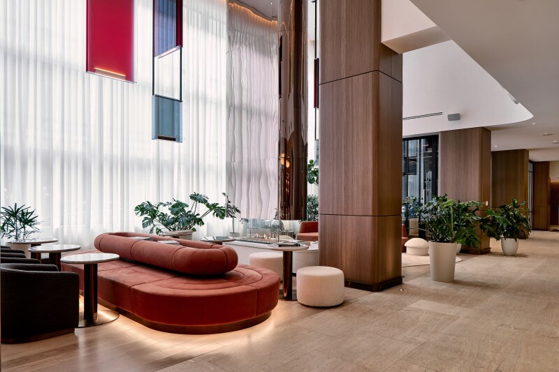 A modern lobby with potted plants, a suspended metallic fireplace, and curvy modern furniture