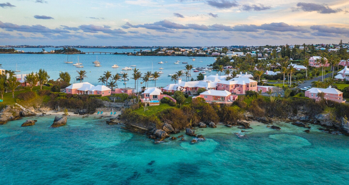 A panoramic view of pink houses and palm trees on a thin stretch of island surrounded by water on either side in Cambridge Beaches, Bermuda
