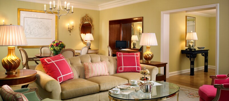 Pale gold interior of California Suite, with large sofa, lit lamps, and large pink pillows
