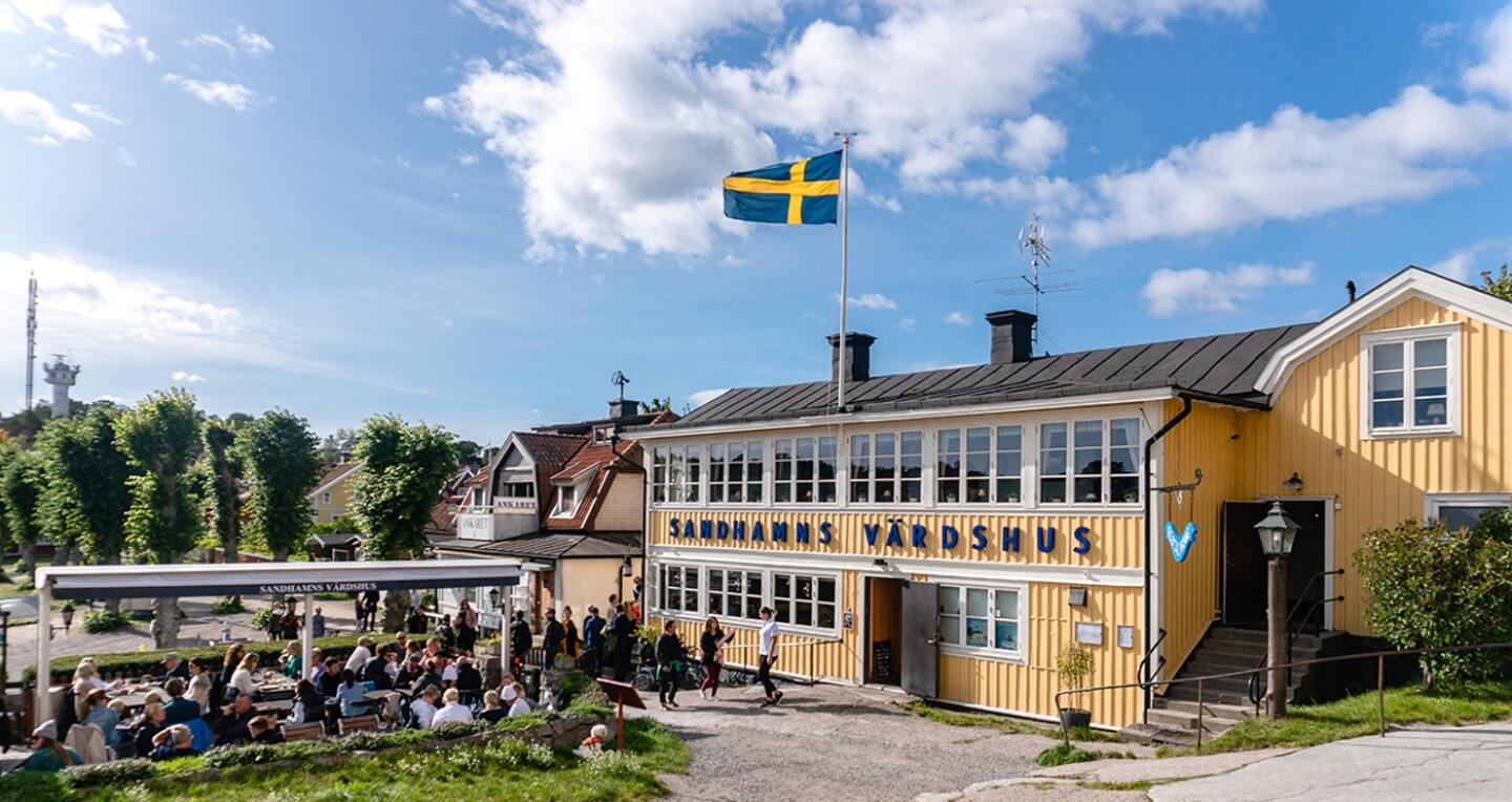 People sit on benches outside a hotel that flies a Swedish flag.