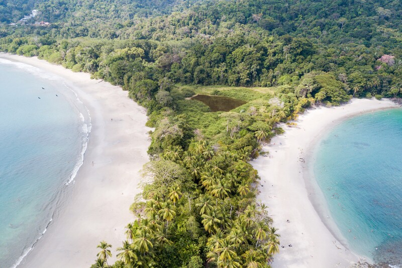 A strip of jungle between two white-sand beaches, each lined with clear light blue waters