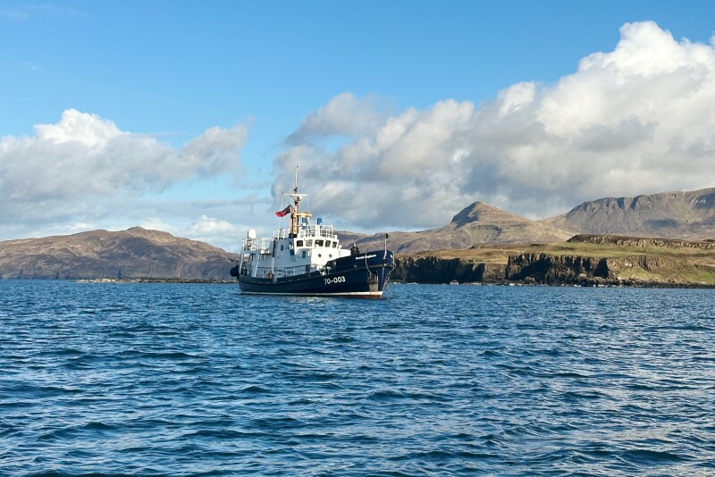 "Gemini Explorer" sailing blue water, with brown hills in background