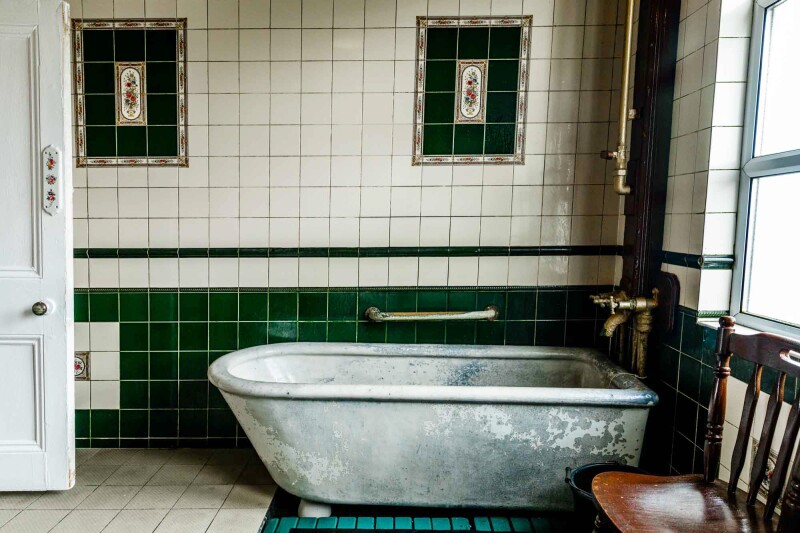 A porcelain-glazed ceramic tub in green-and-white tiled room.