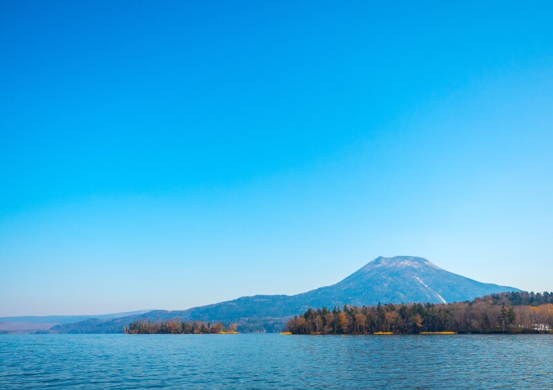 A lake in Japan with autumnal trees and a mountain in the background.