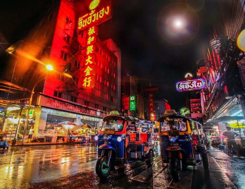 Two tuk-tuks in Bangkok's Chinatown at night, with colorful neon signs and lights