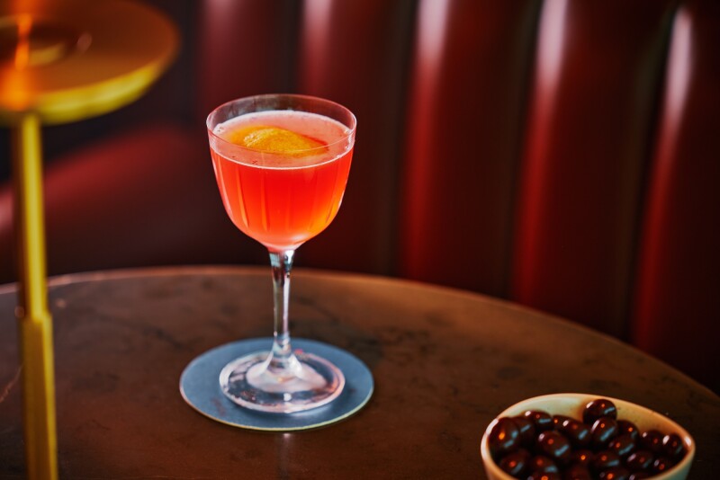 orange-colored cocktail in a wine glass with a floating orange peel on a wooden table in Capital One airport lounge