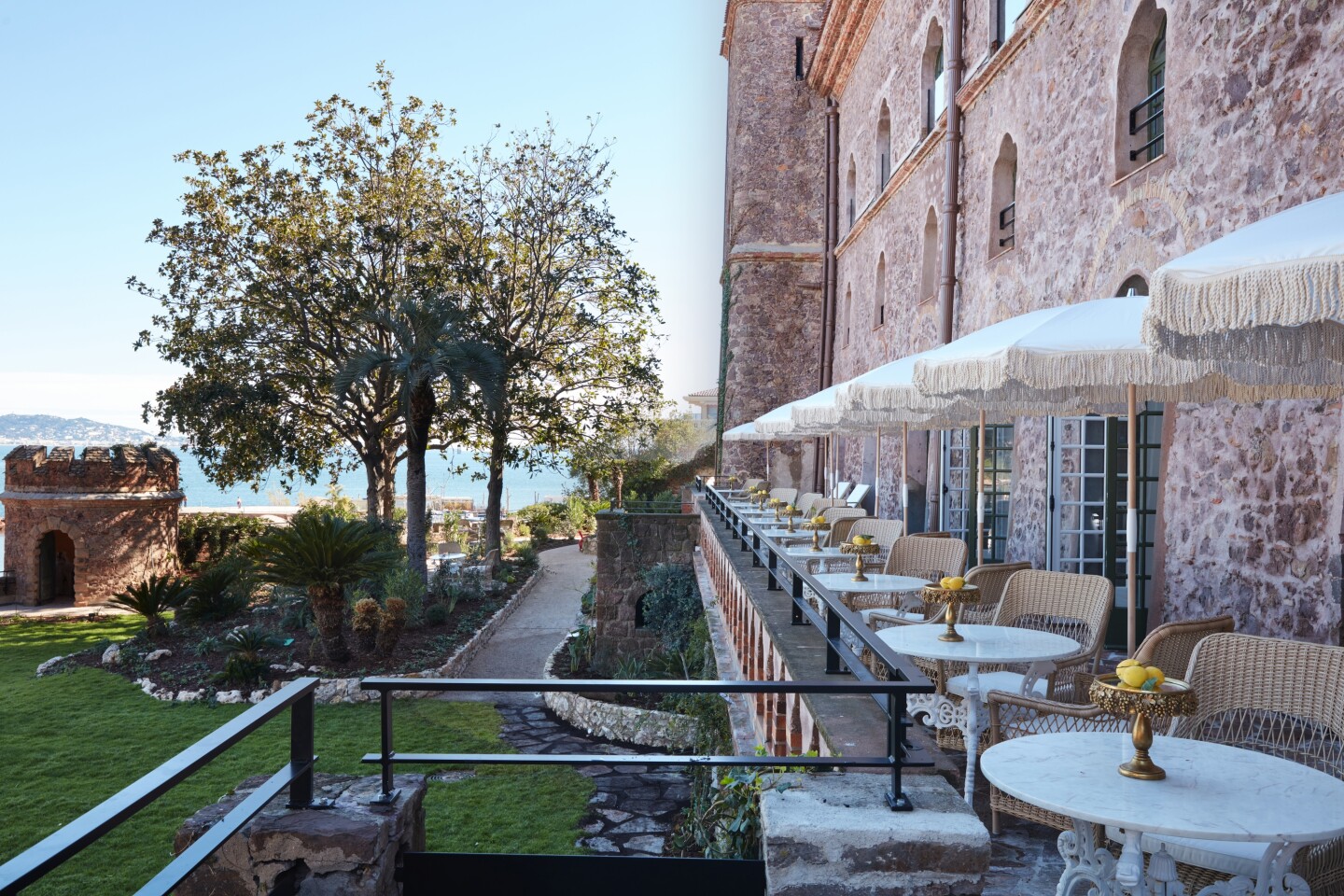 An outdoor dining area at Château de Théoule with row of small, round white table for two shaded by white umbrellas