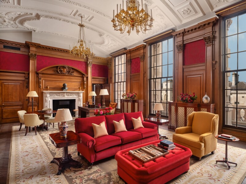 The Haldane Suite at the Raffles London at The Owo features dark wood paneling, a red sofa, and gilt chandeliers.