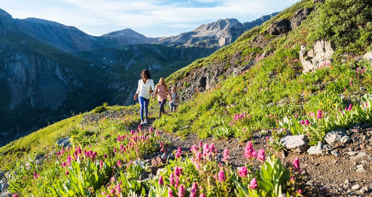 Three women walk on a path through the mountains