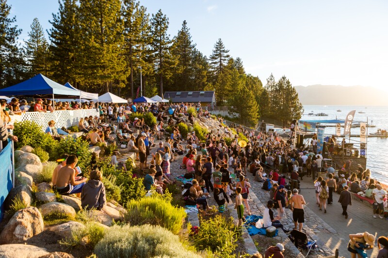 People sitting on outdoor, terraced stone seating in front of South Lake Tahoe, gathered for a free outdoor concert.
