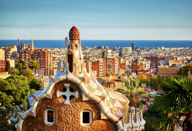 Brown and white Gaudi rooftop in foreground, with expanse of Barcelona in distance
