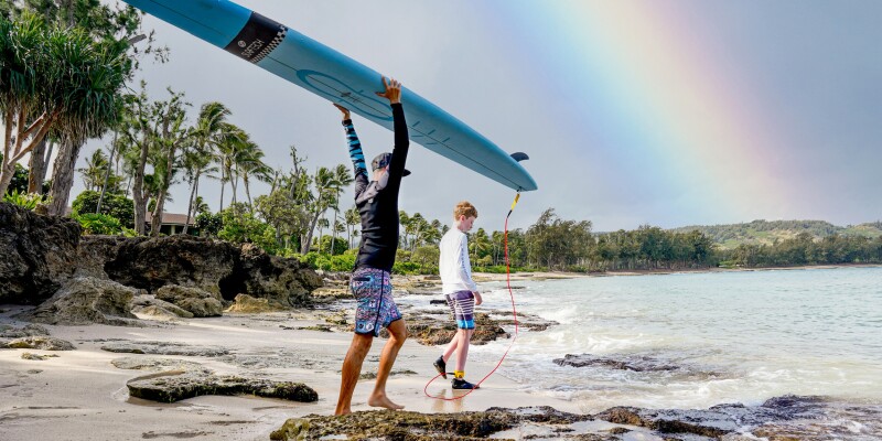 Two people headed into the Pacific Ocean with a surfboard.