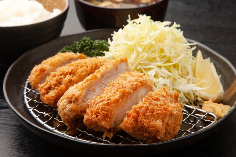 A plate of tonkatsu on a plate with cabbage, parsley, lemon, and mustard