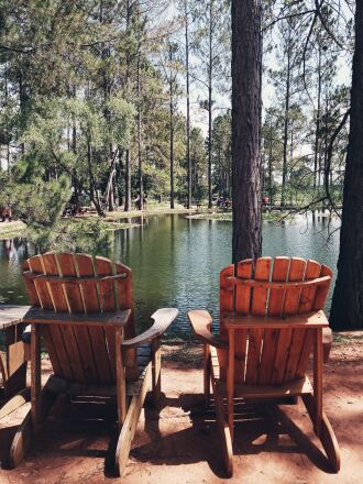 Two empty Adirondack chairs face a pond and cypress trees at Das Peach Haus