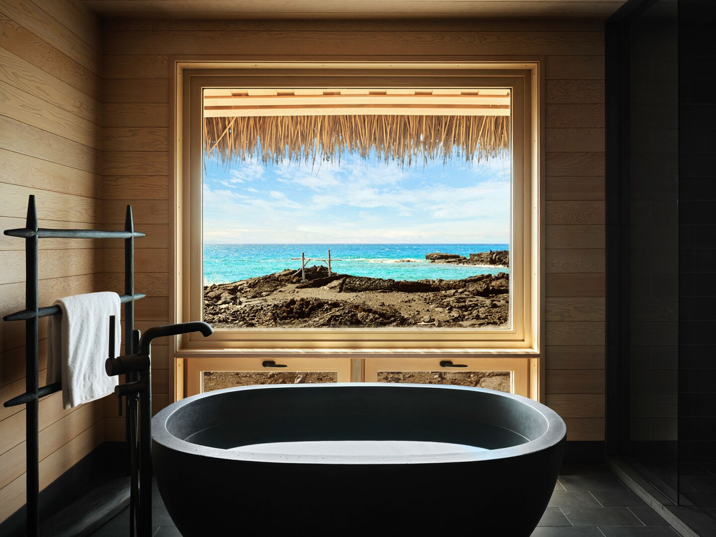 A guest room bathroom at Kona Village, a Rosewood Resort, with large black soaking tub facing the Pacific Ocean